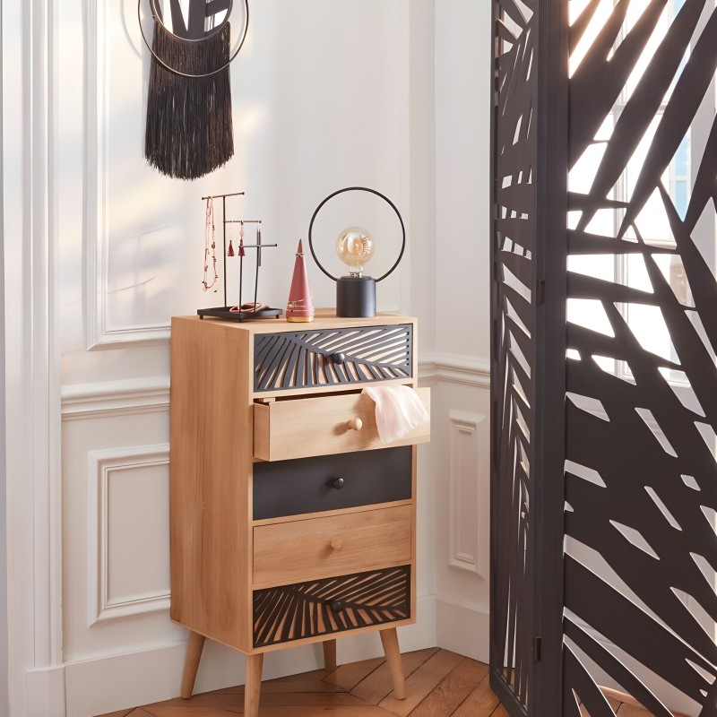 Cómoda de madera clara con cinco cajones en tonos naturales y negro y frentes geométricos decorados en ambiente luminoso