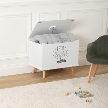 Baúl infantil blanco con tapa abatible y patas de madera con ropa de bebé en su interior en dormitorio