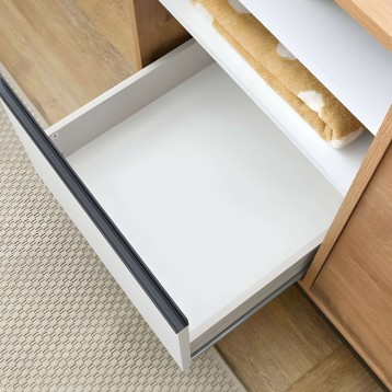 Detalle de cajón abierto en blanco y madera natural con tirador gris y toallas de baño beige en interior
