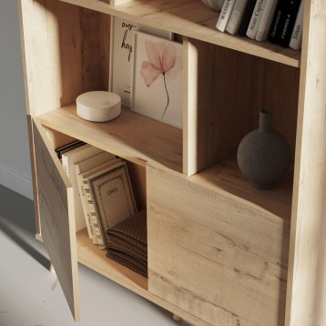Estantería de madera clara con múltiples compartimentos abiertos y puerta inferior decorada con libros y objetos de decoración