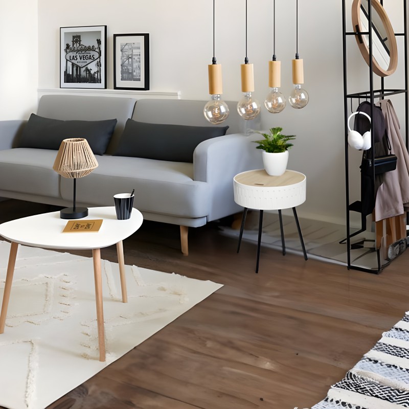 Salón moderno con sofá gris y cojines negros junto a mesita redonda blanca y taburete con tapa de madera