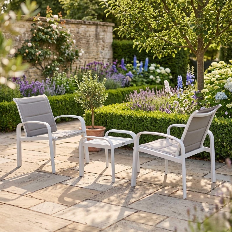 Conjunto de sillones de jardín con estructura blanca y respaldos grises junto a mesa auxiliar en terraza con plantas y flores