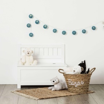 Baúl infantil blanco con respaldo decorado con juguetes y guirnalda de esferas azules en ambiente de dormitorio