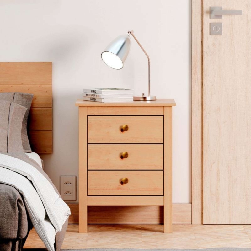 Mesita de noche de madera clara con tres cajones y tirador de madera en dormitorio junto a cama