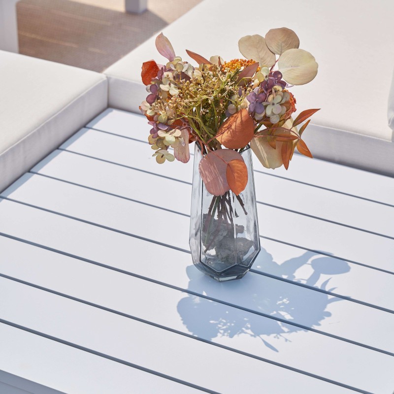 Jarrón de cristal transparente con flores secas en tonos otoñales sobre mesa blanca y azul