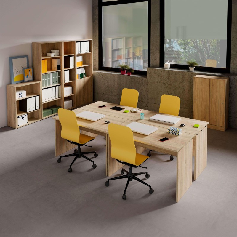 Espacio de oficina con escritorio madera clara y cuatro sillas amarillas ruedas negras rodeadas de estanterías modulares