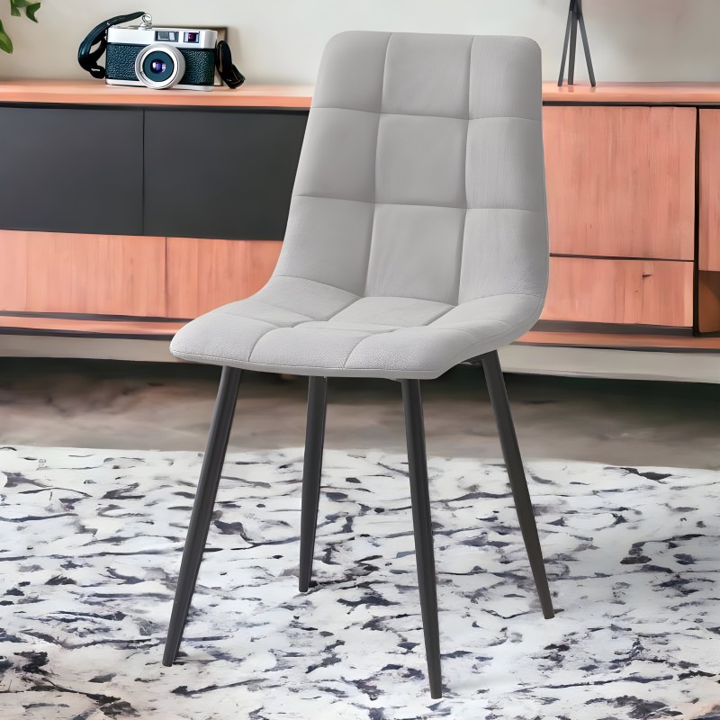Silla moderna tapizada en gris claro con respaldo acolchado y patas metálicas negras en ambiente de interior