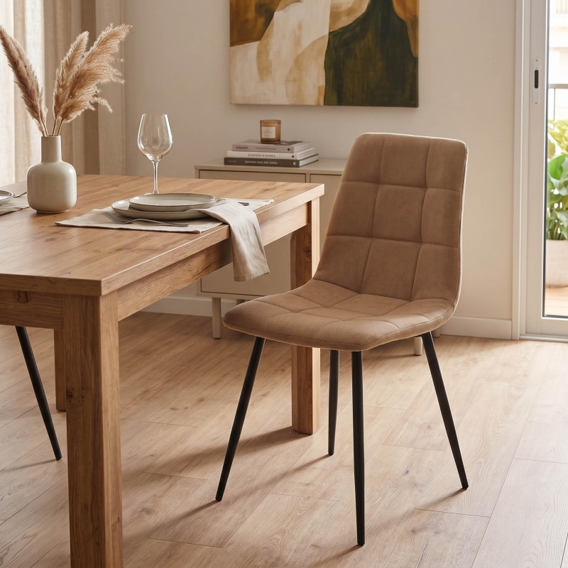 Silla de comedor tapizada en tela marrón con respaldo acolchado y patas metálicas negras junto a mesa de madera clara