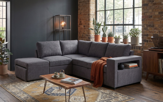 Sofá rinconera gris con chaise longue en salón industrial de ladrillo visto, manta naranja y mesa de madera